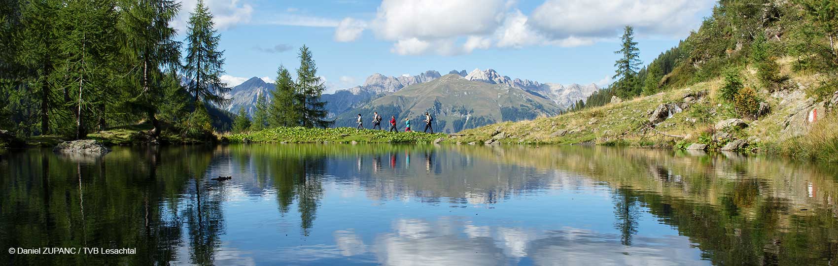 Blick über einen Bergsee auf eine Wandergruppe